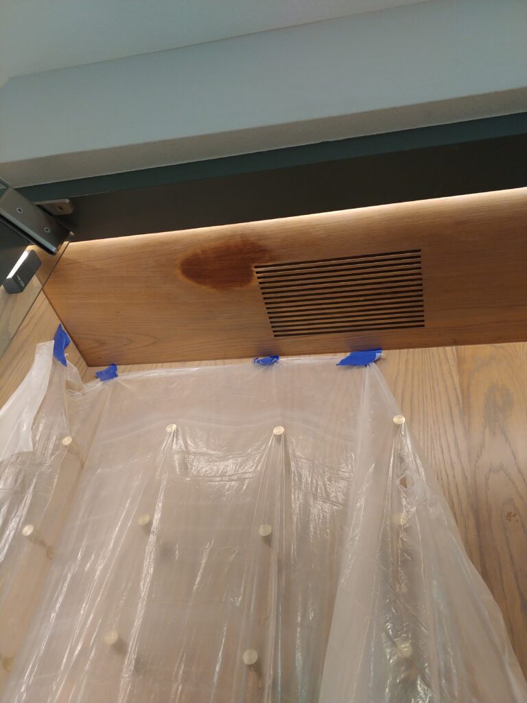Water stain on oak ceiling panel above wine storage vent, caused by an attic leak, before repair
