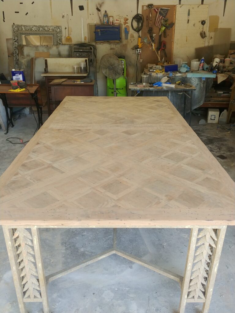 Bare, stripped mahogany parquet table top with diamond pattern in workshop before refinishing