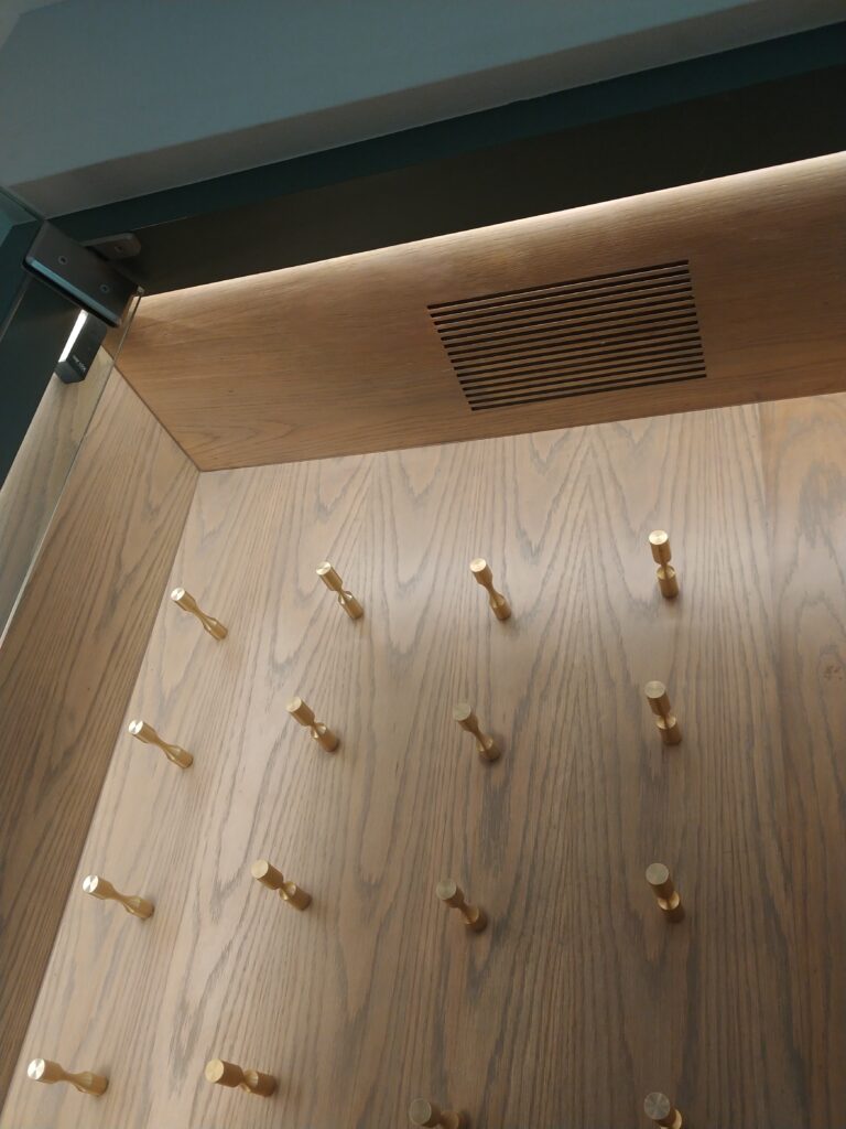 Refinished oak ceiling panel above wine storage vent with brass bottle pegs, after water stain repair