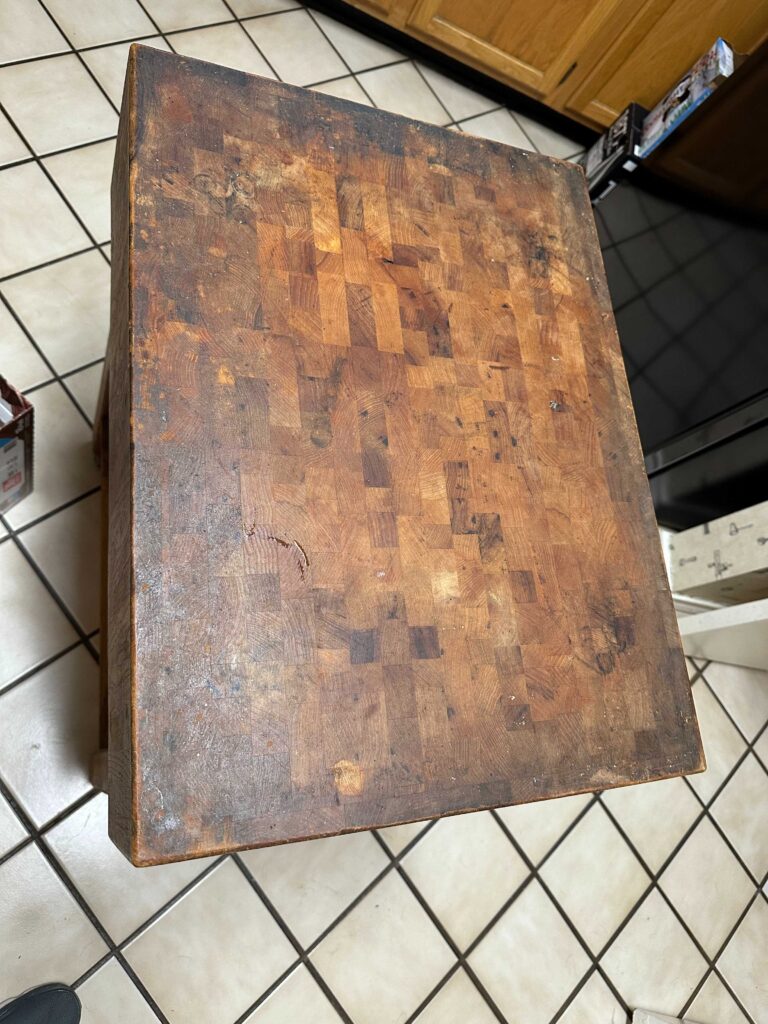 Top-down view of a stained, blotched end-grain butcher block top before restoration in a Dallas kitchen