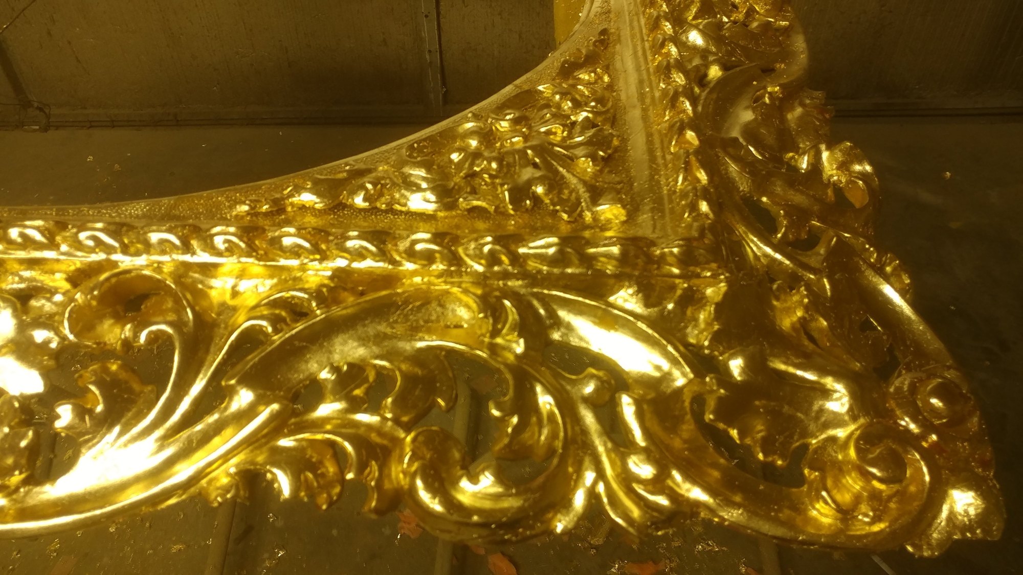 Close-up detail of burnished gold leaf on deeply carved ornament, showing how light moves across the surface
