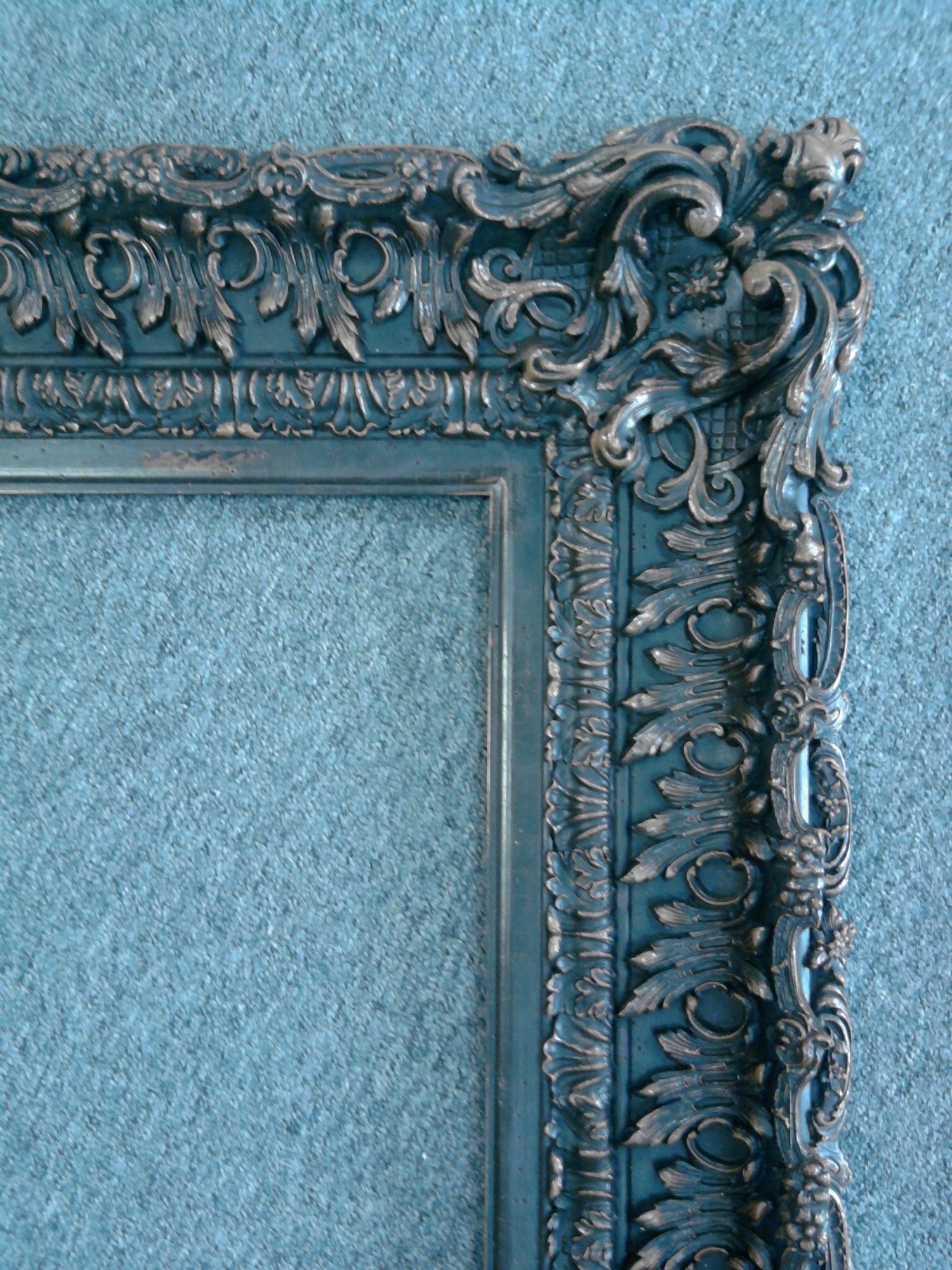 Detail of antique silver leaf gilding on a carved Chippendale-style frame corner, showing the antiqued toning in the recesses